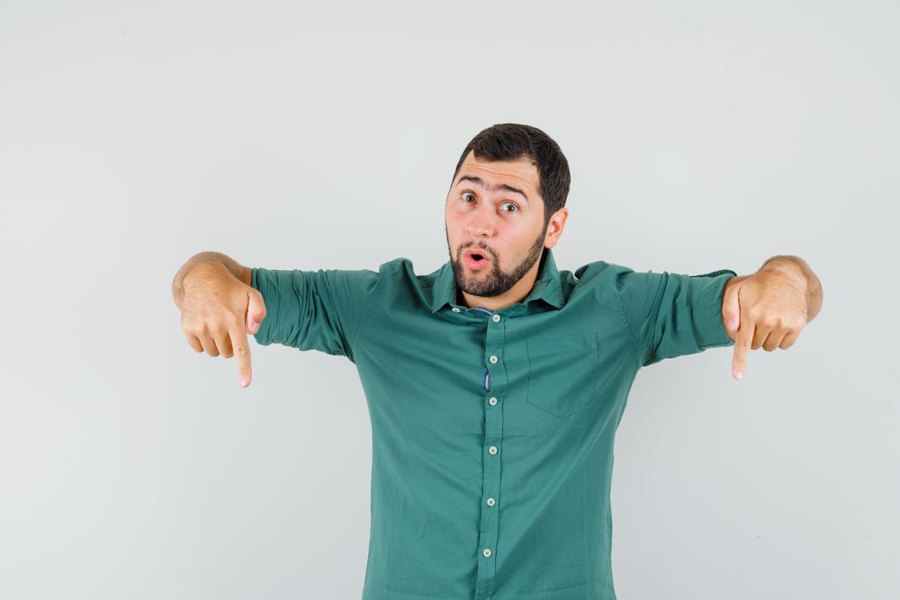 Young male pointing down in green shirt and looking focused. front view.