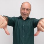 unpleased middle-aged man wearing green t-shirt showing thumbs down isolated on white background